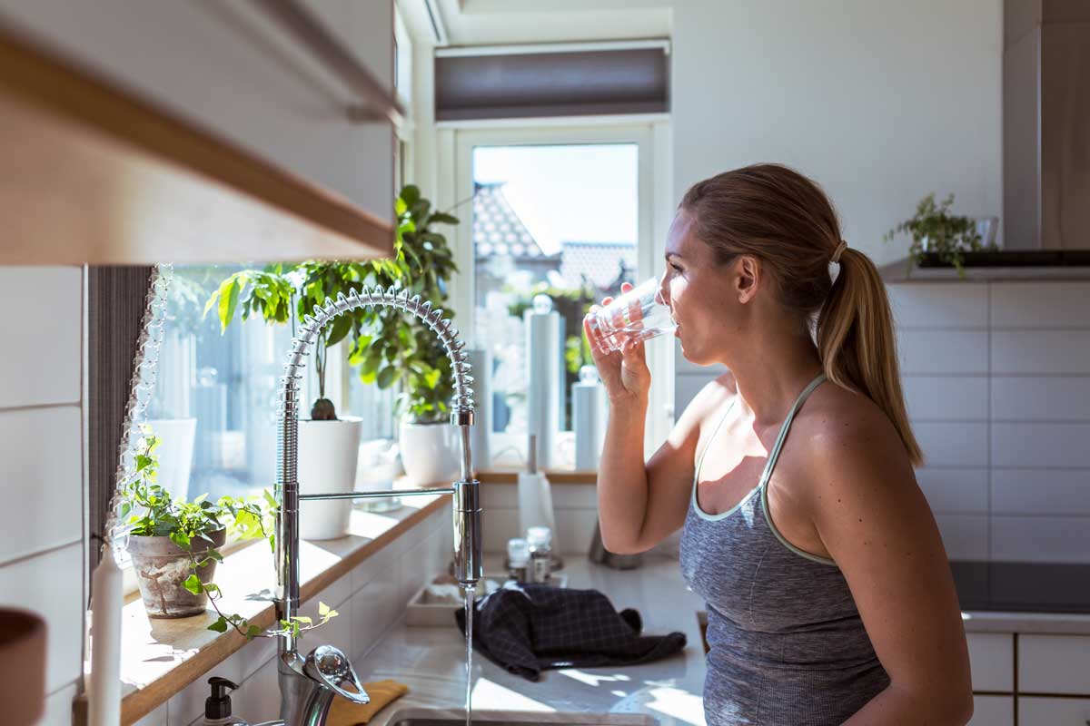 Kvinde, der står i et køkken og drikker et glas vand. Hun er lige uddannet.